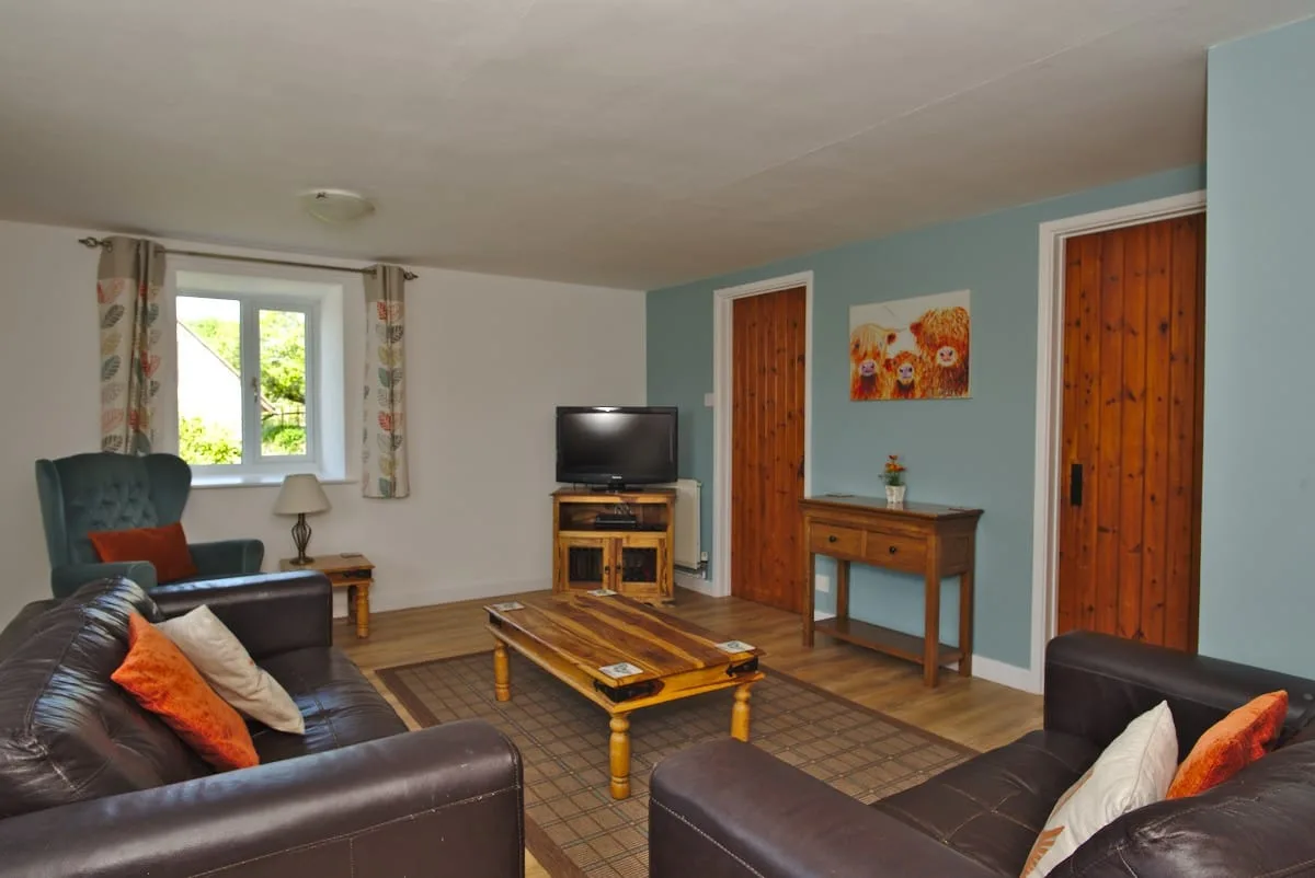 The living room of Granary Cottage which sleeps 6, blue feature wall, leather sofas and television.