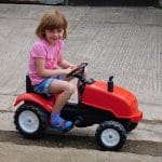 Family farm pictures of a young girl smiling as she rides on a toy tractor.