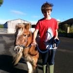 Family farm pictures of a young boy in a red shirt walking Gypsy the Shetland Pony at Lower Campscott.