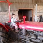 Family farm pictures of a young girl smiling at the camera, sitting in the driver's seat of a vintage red tractor.