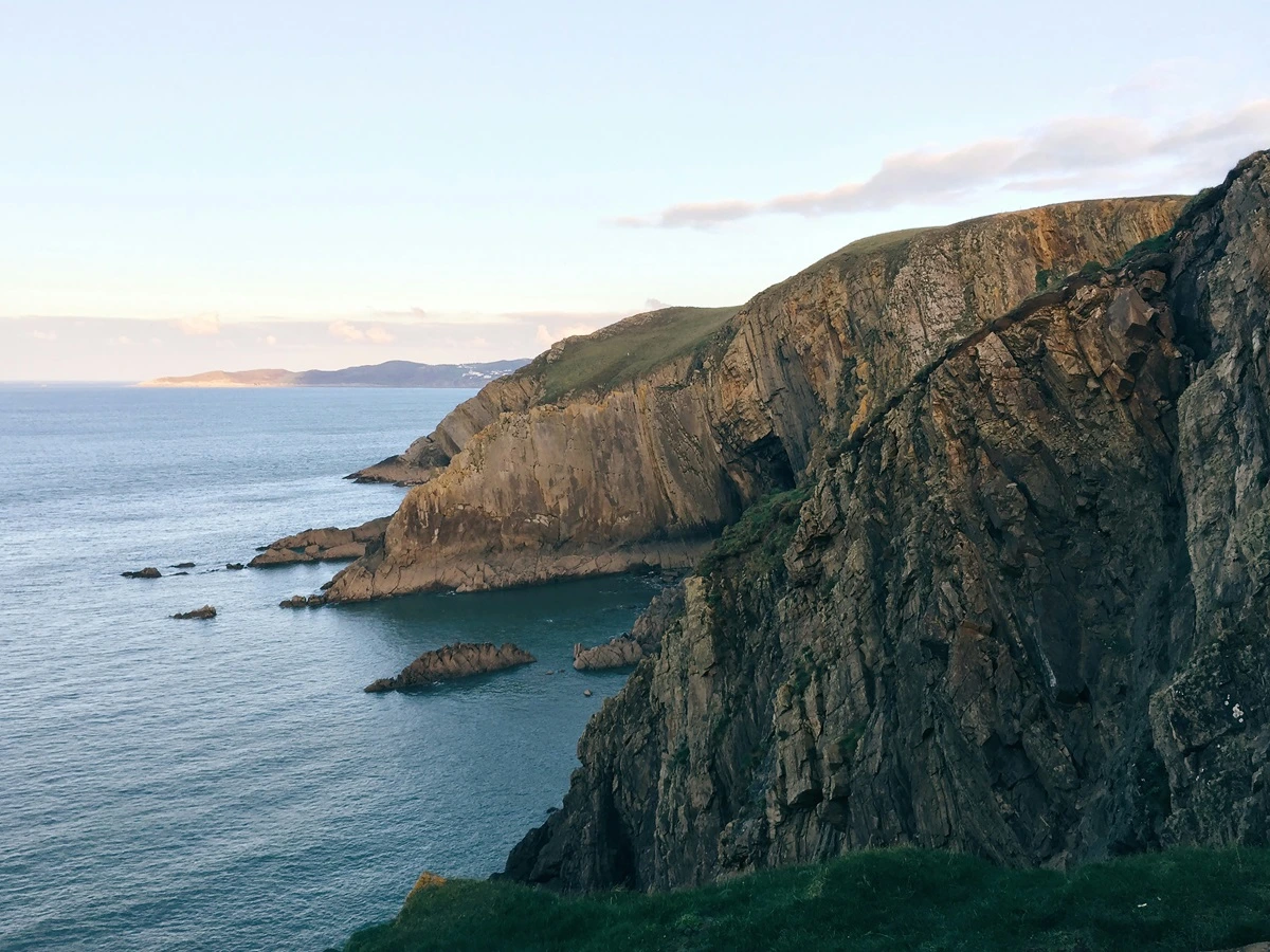 A rocky cliffside in Croyde overlooks a calm sea and clear blue sky, the venue for the Gig Regatta, a family day out.