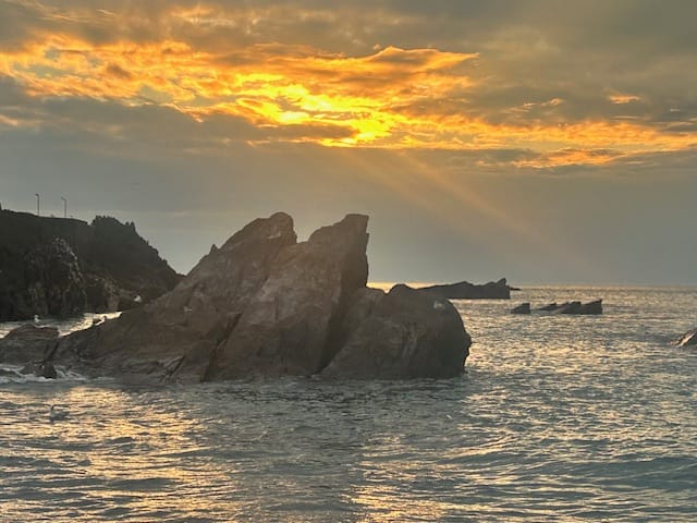 Three rocks jut out of a calm sea, against a deep orange sunset. Popular destination for October half term getaways.
