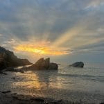 Rocks in a calm sea against a halo of light from a sunset.