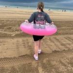 A young girl with an inflatable ring walks on the beach.