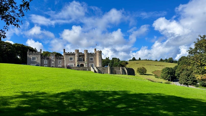 A landscape shot of Watermouth castle, green grass under a cloudy blue sky.